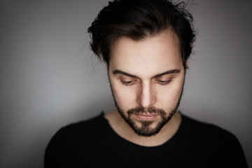 Closeup portrait of handsome young fashion man in tshirt poising while standing on empty gray background. Horizontal