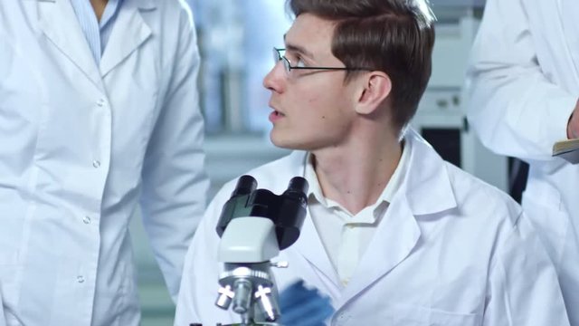 Medium shot of group of chemists in lab coats working in laboratory and discussing research details