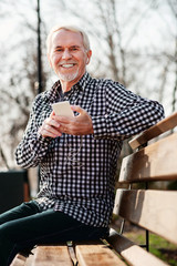 Mood for music. Low angle of merry senior man looking at camera and listening to music