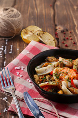 shrimp mussels and squid on frying pan close up on dark wood back with lemon