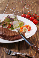 steak with vegetables on dark wooden background with cherry tomato and cutlery