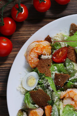 Caesar salad with shrimps and cherry tomato on wood background