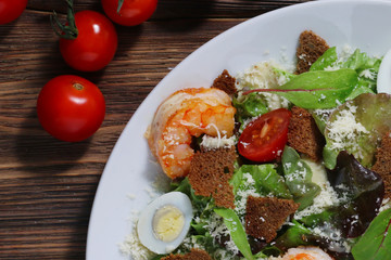 Caesar salad with shrimps and cherry tomato on wood background