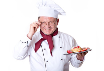 Chief confectioner is holding a dessert with strawberries on a plate.