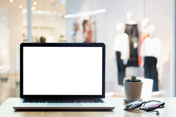 Laptop with blank screen on table. Clothes shop  blurred background.