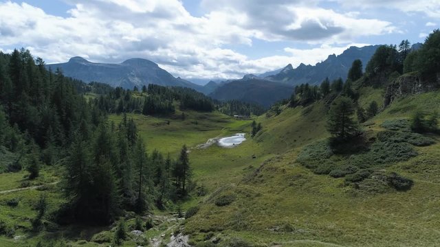 aerial forward over pine forest woods hill to alpine mountain valley in sunny summer with clouds.Alps outdoors green nature scape mountains wild aerial establisher.4k drone flight establishing shot