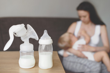 Bottle and breast pump with breast milk on the background of mother holding in her hands and breastfeeding baby. Maternity and baby care. - 206029324