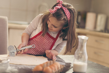 Little girl cutting dough for rolls