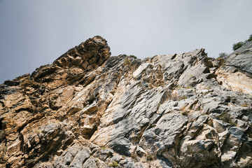 Big mountain cliff under cloudy sky close-up. Beautiful rocky gray textured background with vegetation. Majestic nature.