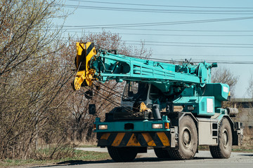 Obraz premium Large heavy car with crane is driving along road under wires.
