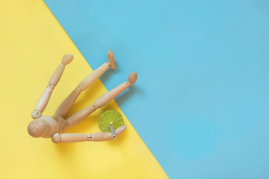 Wooden doll with fresh citric drink on yellow as sand beach and blue as water. Concept tan and beach.