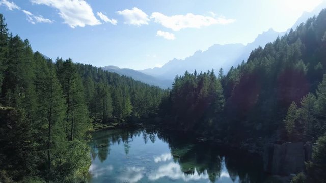 aerial forward over blue alpine lake revealing mountain forest valley in sunny summer with clouds.Europe Alps outdoors green nature scape mountains wild establisher.4k drone flight establishing shot