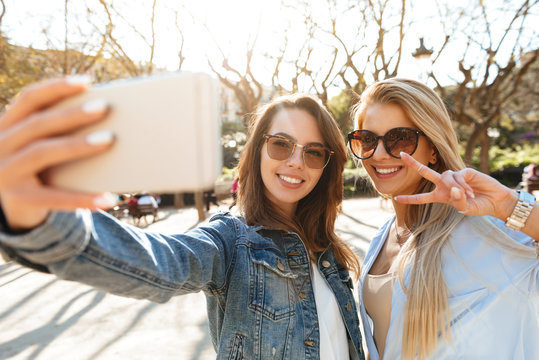 Two amazing smiling women friends make selfie by mobile phone.