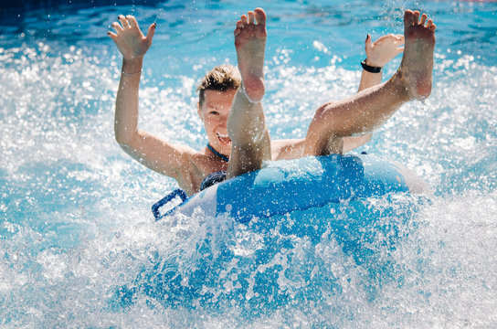 Funny girl taking a fast water ride on a float splashing water. Summer vacation with water park concept.