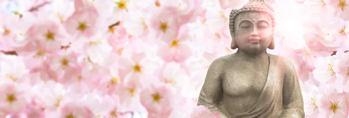 Foto auf Acrylglas Buddha Buddha-Skulptur im Sonnenschein unter den blühenden Kirschblüten