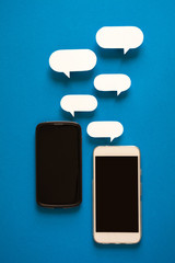 Smartphones with paper speech bubbles on blue background. Communication concept. Top view. Copy space. Paper composition