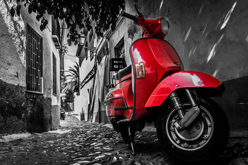 Scooter vespa rouge garé dans une vieille rue pavée vide