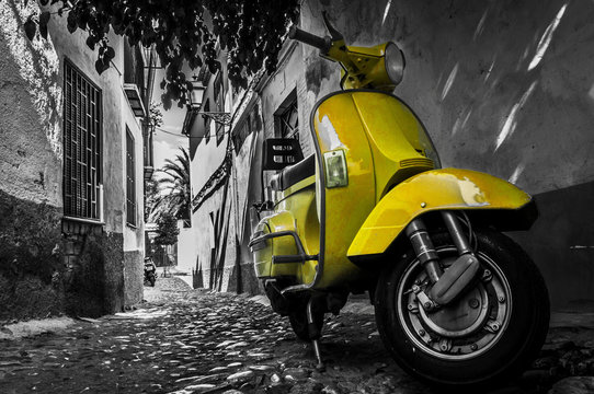 Yellow vespa scooter parked in an old empty paved street
