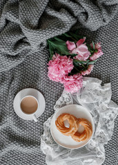 A cup of coffee with sweets and peonies on a gray background