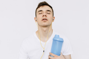 A young man is tired after playing sports. After training. Listens to music and holds a shirek in his hand. Іsolated white background