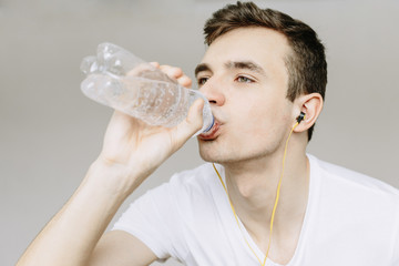 Young guy drinks water after a workout. Thirst after water training. Іsolated gray background