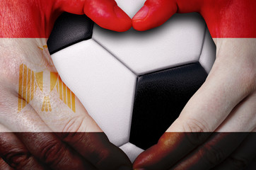 Hands painted with an Egypt flag forming a heart over soccer ball background