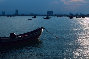 Naklejka premium wooden boat. sunset light. dark blue sea. city silhouette on horizon