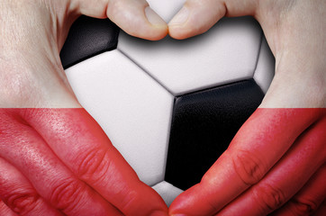 Hands painted with a Poland flag forming a heart over soccer ball background