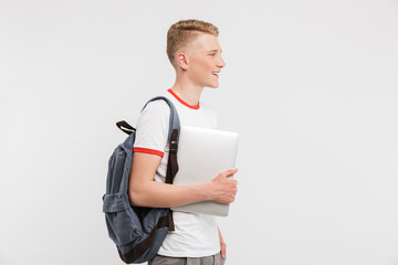 Image of male student 16-18 years old wearing casual clothing and backpack walking with holding laptop in hand, isolated over white background