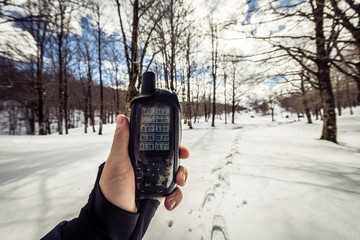 Close- up of a man's hand holding a GPS in a snowy forest. Checking GPS information. Footprints in...