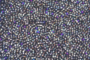 Glamorous background of shades of silver. A scattering of silver, purple, pink, blue and red shiny balls. Imitation of diamonds. Beautiful shiny texture. Glitter glass balls sewn on a velvet belt. 