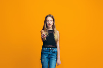 The happy teen girl pointing to you, half length closeup portrait on orange background.