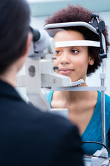 Optician measuring women eyes with refractometer in optician shop