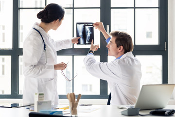 Experienced male orthopedist helping his female colleague with the interpretation of an X-ray of...