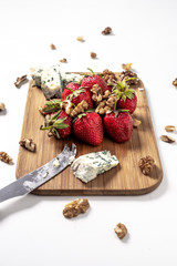 Strawberries in focus on wooden board with blue cheese and nuts seeds sprinkled around