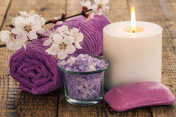 Sea salt in glass bowl, towel for bathroom procedures with flowering branch of apricot tree, soap and  burning candle