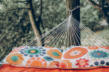 Obraz premium pillows on colorful stylish travel hammock in summer sunny park. resting, camping and relaxing outdoor, summer vacation and holiday. space for text. wanderlust and adventure