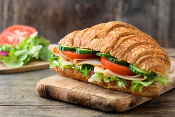 Croissant sandwich with cheese, ham and vegetables on wooden table