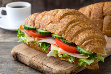 Croissant sandwich with cheese, ham and vegetables on wooden table