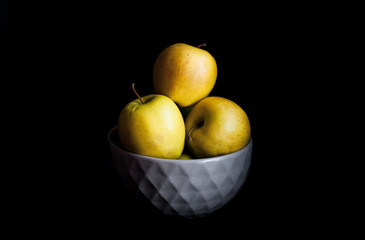 Bowl of yellow apples. On black background.