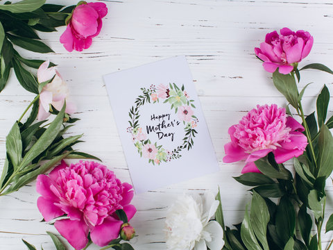 Pink and white peonies around postcard for Mother's Day on a wooden background.