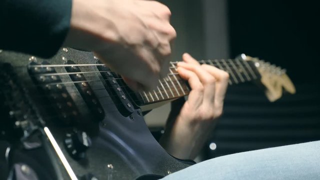 Close up fingers of guitarist at the strings. Mens arms plays solo of rock music. Hands of male musician playing at electric guitar. Beautiful black background at studio. Slow motion Close up
