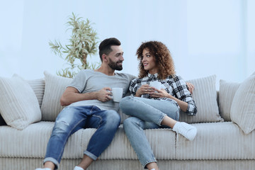 Obraz premium Beautiful couple holding a cup of drink while sitting on the couch at home