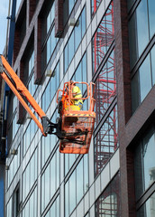Fototapeta premium construction worker on an orange elevated platform on a large modern building site