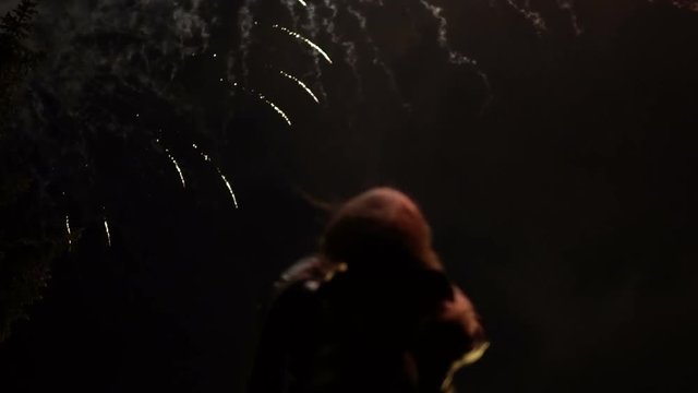The girl takes pictures of fireworks on a mobile phone. Silhouette on the background of the sky illuminated by lights.