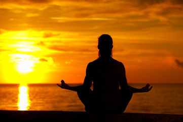 Silhouette of relaxed yong woman sitting in yoga lotus pose against sea background on warm sunny day during sunset
