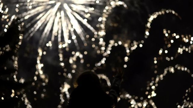 The girl takes pictures of fireworks on a mobile phone. Silhouette on the background of the sky illuminated by lights.