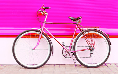 Fototapeta premium Retro pink bicycle stands over colorful pink background