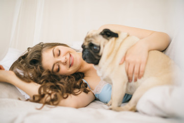 Lovely family weekend. Woman relaxing in bed with pug dog. Sunny day