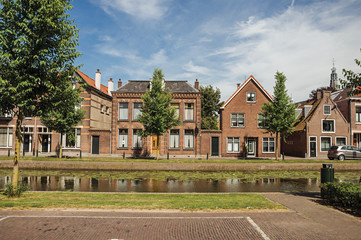 Fototapeta premium Tree-lined canal with streets on the banks and brick houses on sunny day in Weesp. Quiet and pleasant village full of canals and green near Amsterdam. Northern Netherlands.